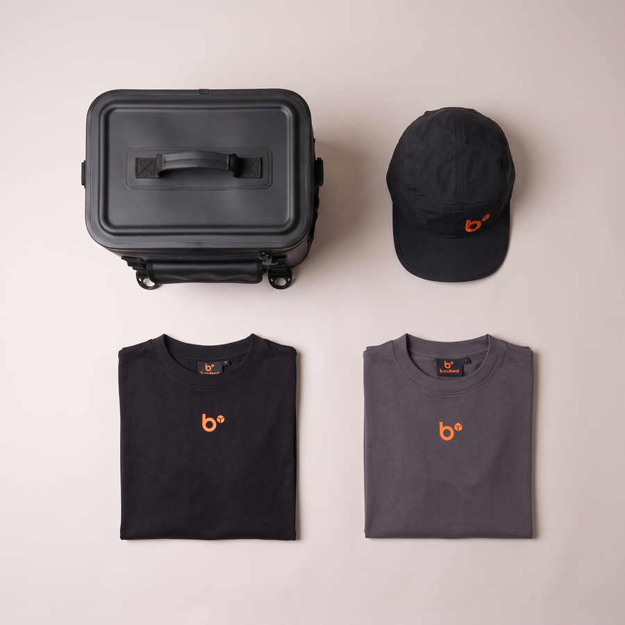 Flat lay of THE FULL KIT: THE CUBE lunchbox, work cap, black work tee and dark grey work tee